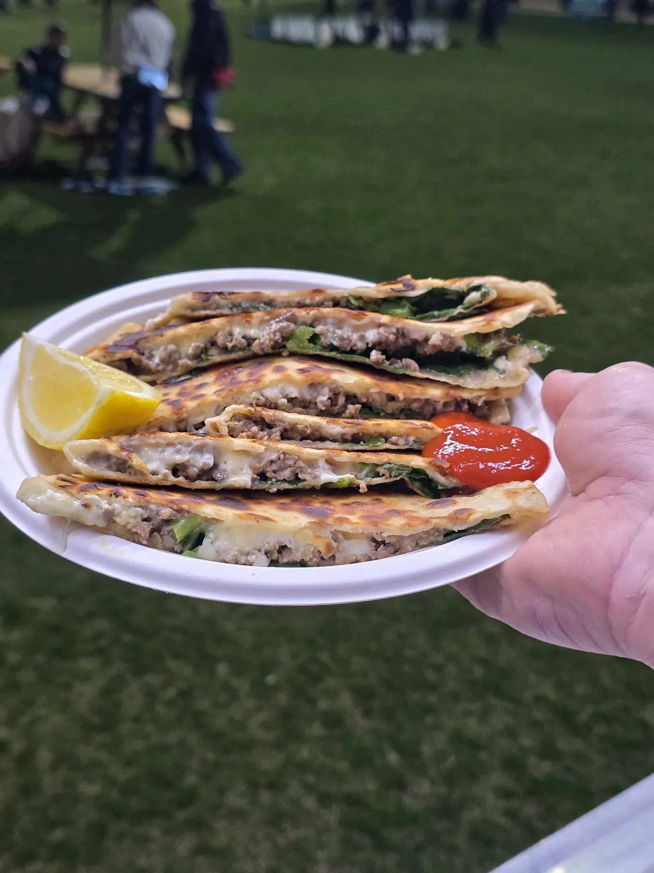 A plate of hand-rolled Uz Gözleme with a lemon wedge and chilli sauce, held up at an Adelaide market