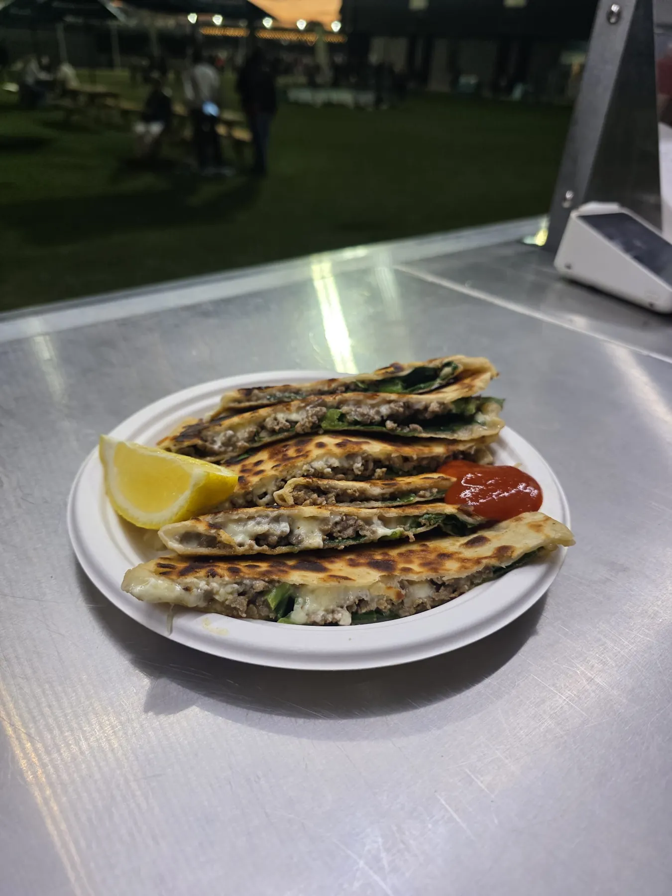 Gözleme cut into wedges on a plate with lemon and chilli sauce at a night market