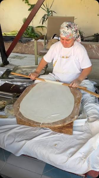 Black and white photograph of a grandmother rolling a large sheet of gözleme dough