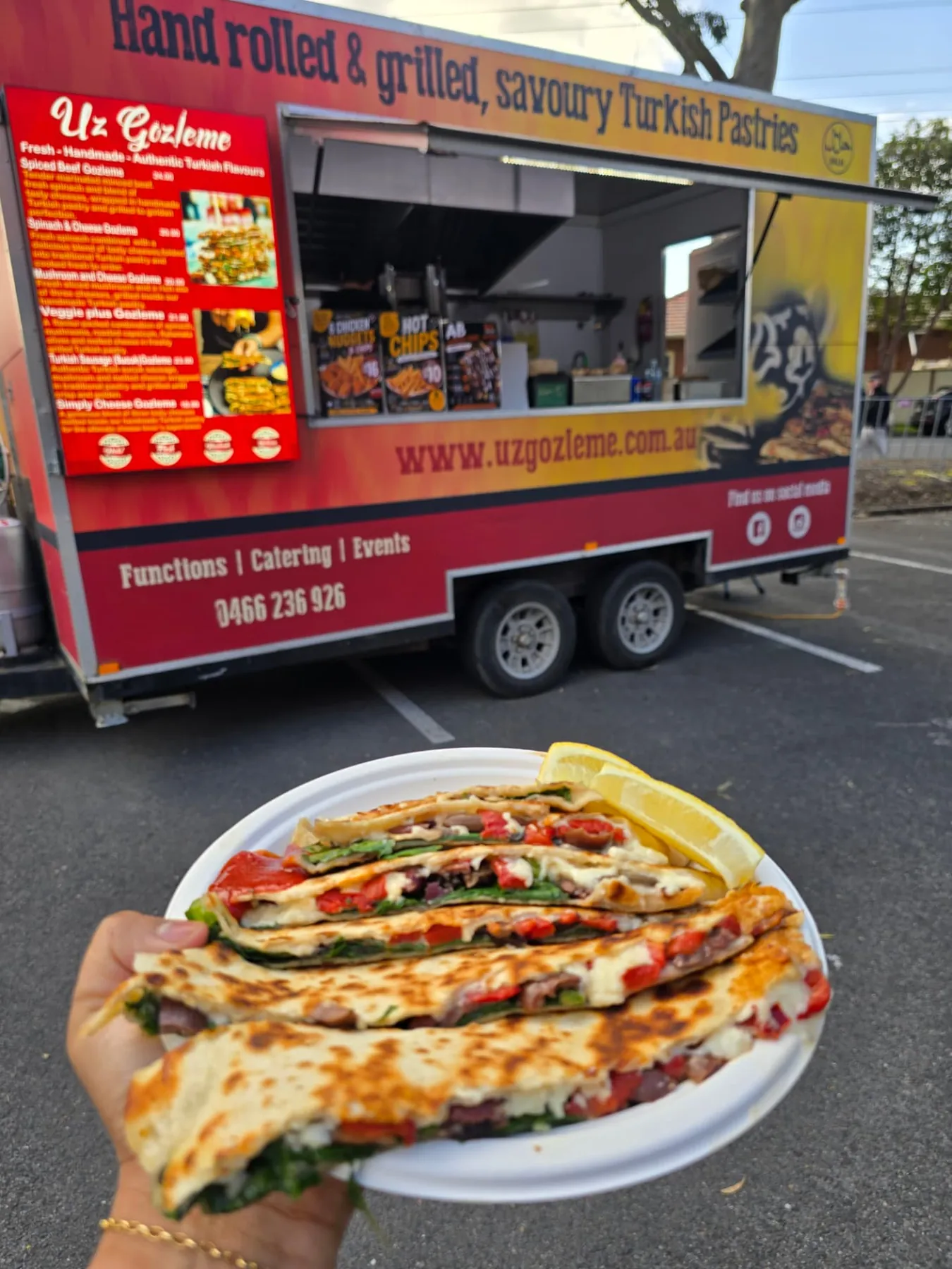 Veggie plus gözleme on a plate held in front of the red Uz Gözleme trailer